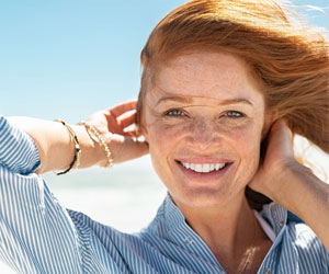 Eine Frau steht im Wind in der Sonne und lächelt in die Kamera.