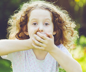 Ein Mädchen im Grünen, es hält sich mit aufgerissenen Augen mit beiden Händen den Mund zu. 