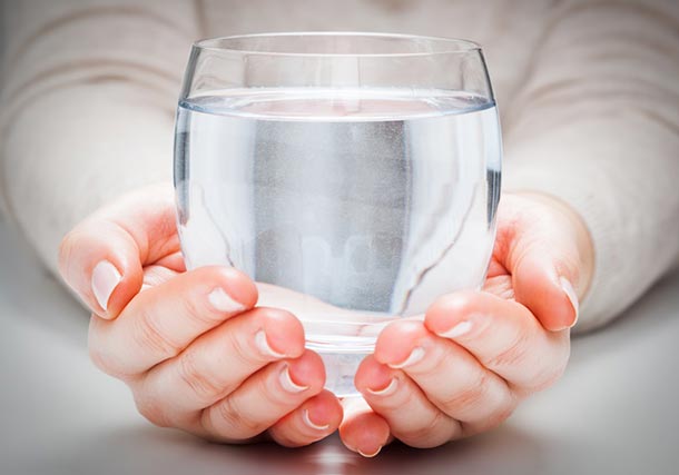 Frauenhände halten ein grosses rundes Glas Wasser.