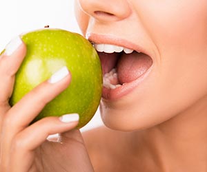 Eine Frau beisst mit gesunden Zähnen in einen grünen Apfel.