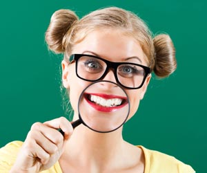 Eine junge Fraut mit Brille hält sich eine Luppe vor den Mund. Man sieht ihre Zähne vergrössert im Bild.