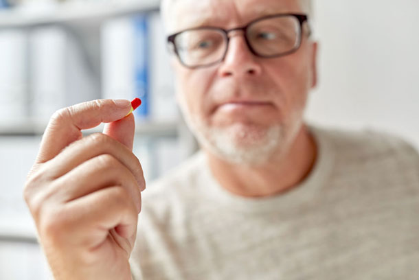 Un homme regarde d'un œil critique une pilule qu'il tient dans sa main.